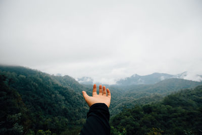 Cropped hand gesturing against mountains