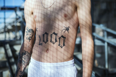 Midsection of shirtless man with tattoo in sunlight at home