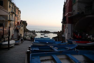 Boats moored on sea by buildings against sky at sunset