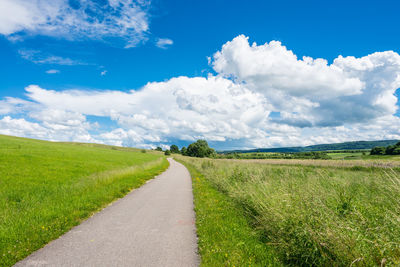 Footpath amidst grassy field against cloudy sky