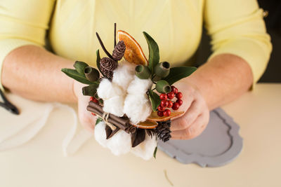 Woman holds small bouquet with cotton flowers and dry orange slices above table