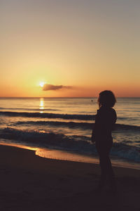 Silhouette woman standing at beach during sunset