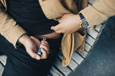 Midsection of man injecting insulin while sitting on bench