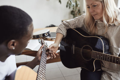 Blond female tutor looking at male student playing guitar in classroom