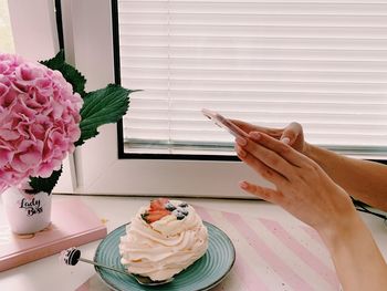 Midsection of woman holding pink flower on table