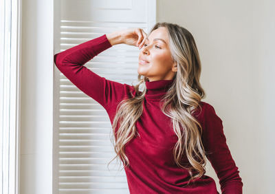  young beautiful woman with blonde long curly hair in bordo sweater in bright interior