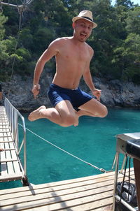 Full length of shirtless man jumping over pier