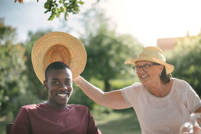 Happy grandmother holding straw hat over grandson during garden party on sunny day