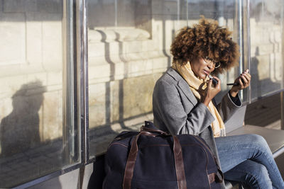 Woman applying lipstick while sitting at bus stop