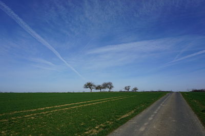 Road amidst green landscape against blue sky