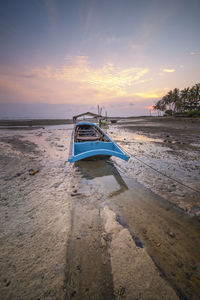 Boat moored on beach against sky during sunset