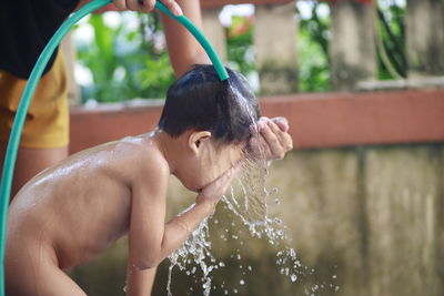 Shirtless boy taking shower outdoors