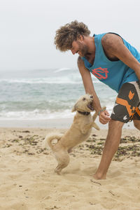 Young man with dog playing on beach