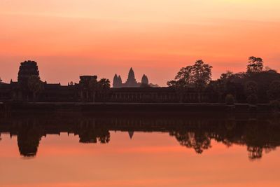 Reflection of historic temple in lake against orange sky