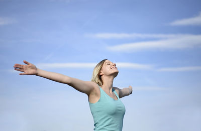 Woman with arms outstretched standing against sky