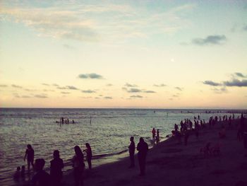 Silhouette people standing on beach against sky during sunset