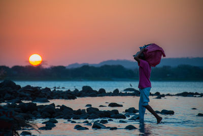 Rear view of man standing at beach during sunset