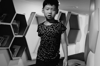 Portrait of boy standing against shelf at home