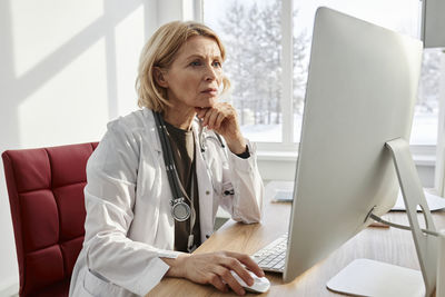 Doctor with hand on chin using desktop pc at desk in clinic