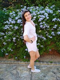 Full length portrait of beautiful woman standing by flowers on footpath at park