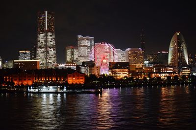 Illuminated buildings by river against sky at night