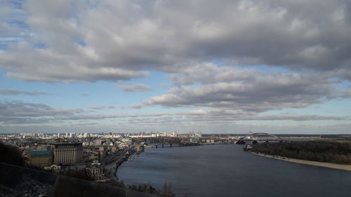 High angle view of buildings by river against cloudy sky