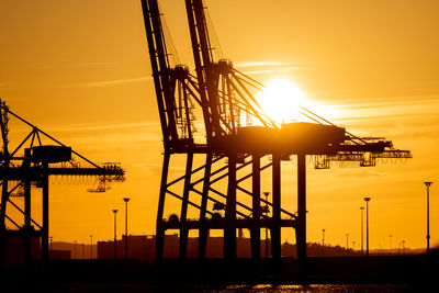 Silhouette cranes against sky during sunset