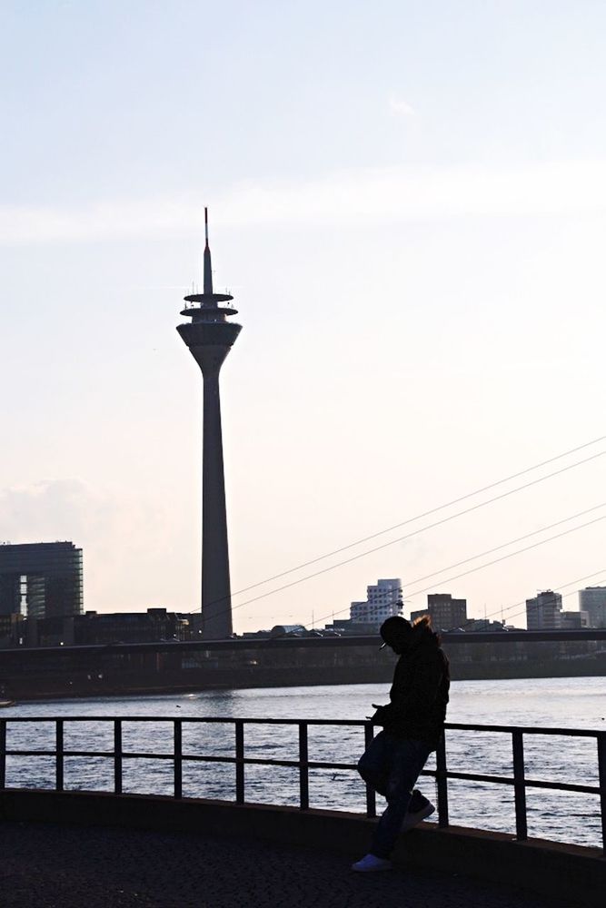 built structure, architecture, railing, lifestyles, men, leisure activity, silhouette, standing, building exterior, sky, water, city, rear view, connection, bridge - man made structure, river, full length