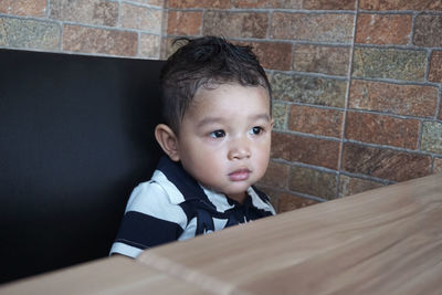 Cute boy looking away while sitting against wall