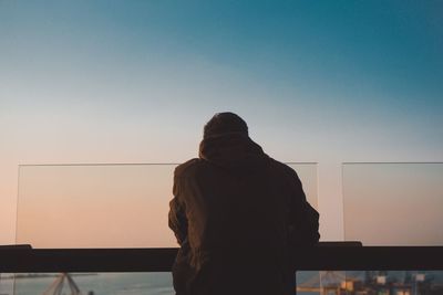 Rear view of silhouette man standing by railing against clear sky