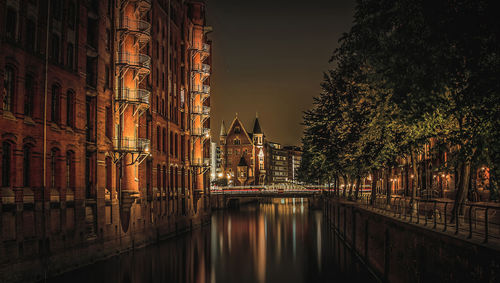 Illuminated buildings by canal against sky at night