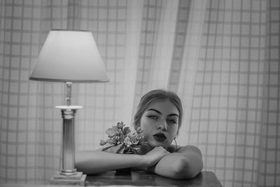 Portrait of woman sitting at table against curtain