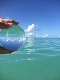 Midsection of person holding sea against blue sky