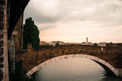 Arch bridge over river amidst buildings against sky