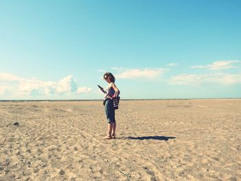 Woman using phone while standing on sand at desert against sky 