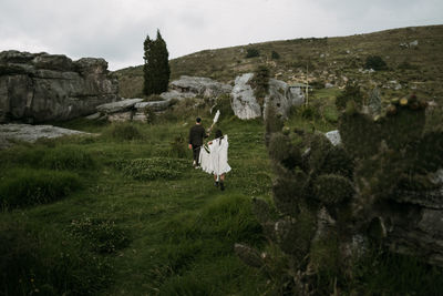 Back view of trendy bride and groom standing near rock on wedding day