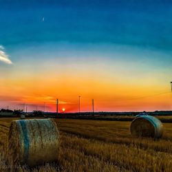 Hay bales on field against sky during sunset