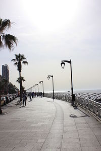 Street lights on footpath by sea against sky