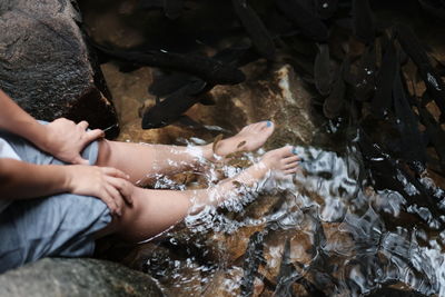 Low section of woman sitting on rock by water