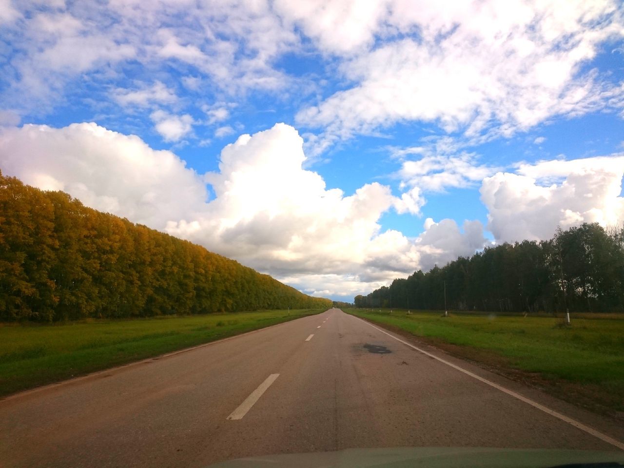 road, transportation, the way forward, road marking, sky, tree, tranquil scene, diminishing perspective, landscape, cloud, long, tranquility, vanishing point, solitude, cloud - sky, day, blue, outdoors, nature, country road, cloudy, countryside, cumulus cloud, white line, non-urban scene, grass area, remote, green color, surface level, dividing line, beauty in nature, scenics, straight