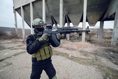 Army soldier aiming while standing against built structure