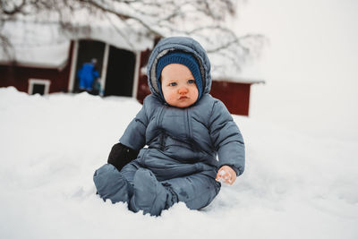 Adorable baby sitting on snow touching snow for first time at the farm