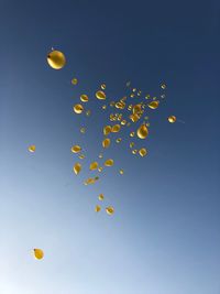 Low angle view of yellow balloons flying against blue sky