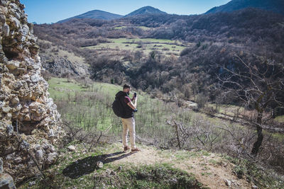 Rear view of hiker standing on rock against sky