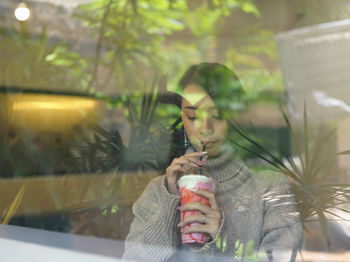 Portrait of young woman drinking glass window