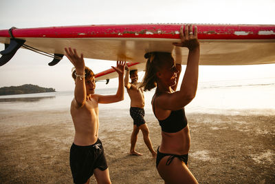 Happy family carrying paddleboards on heads while walking at beach during sunset