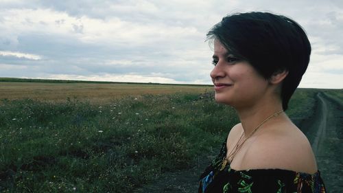 Smiling woman looking away while standing on land against sky