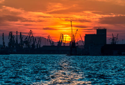 Silhouette sailboats on pier at harbor against sky during sunset