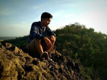 Young man sitting on rock against trees