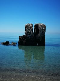 Built structure on rocks by sea against clear blue sky